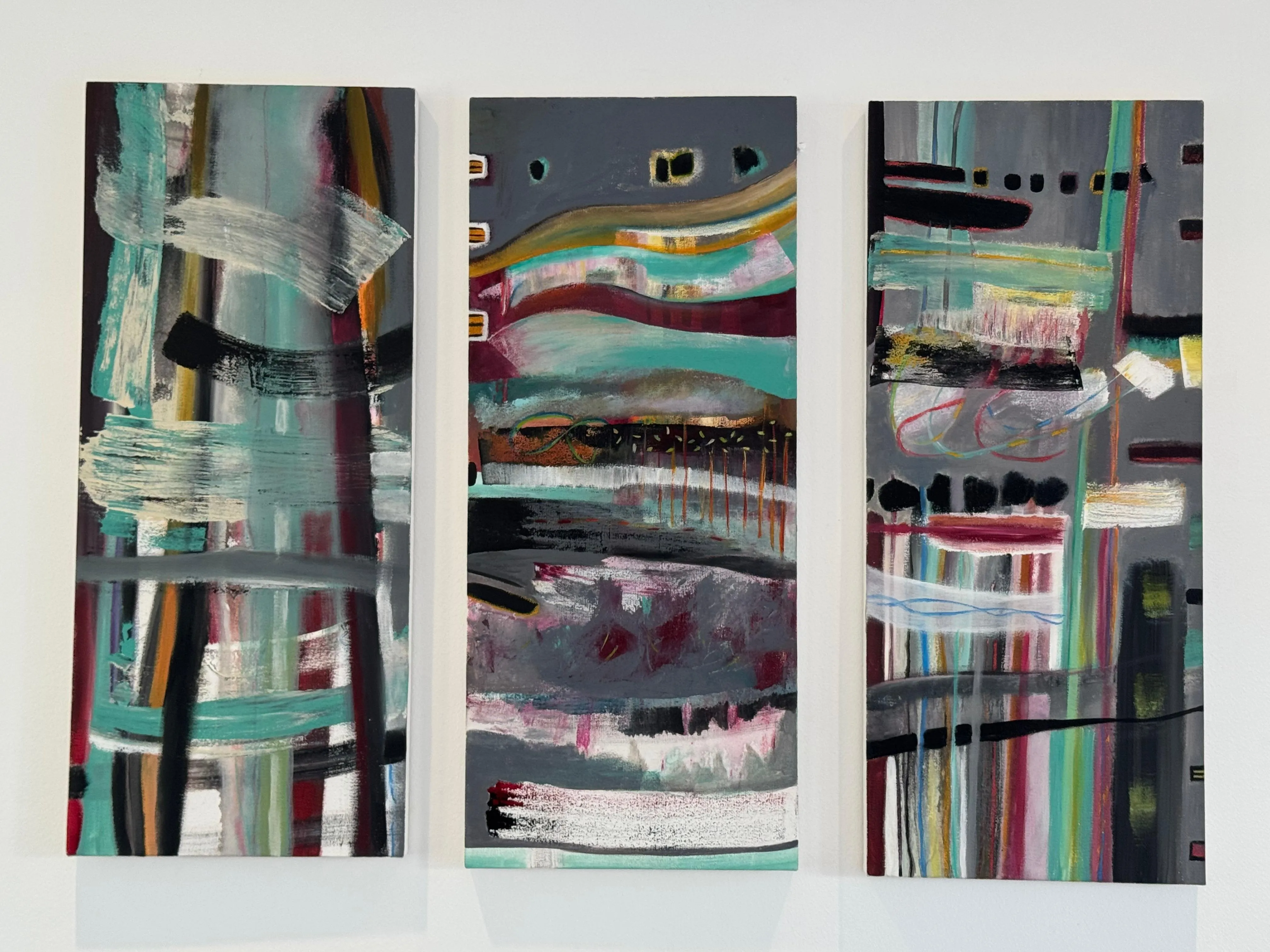 A triptych of tall narrow panels on silver-grey grounds, swept with horizontal bands of teal, magenta, ochre and white, threaded with thin ribbons of coloured line and runs of dripped paint - layered and rhythmic, like three measures of the same music.